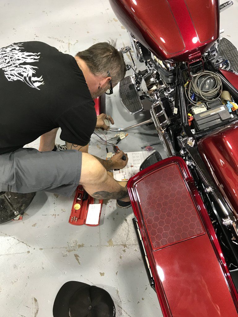 worker detailing rear view of customized red and chrome motorcycle in garage with dakota kustomz graffiti art