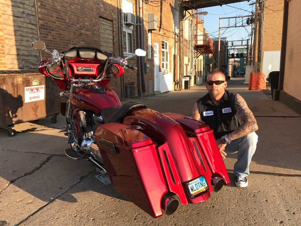 owner travis feist squatting near rear view of customized red and chrome motorcycle in alley