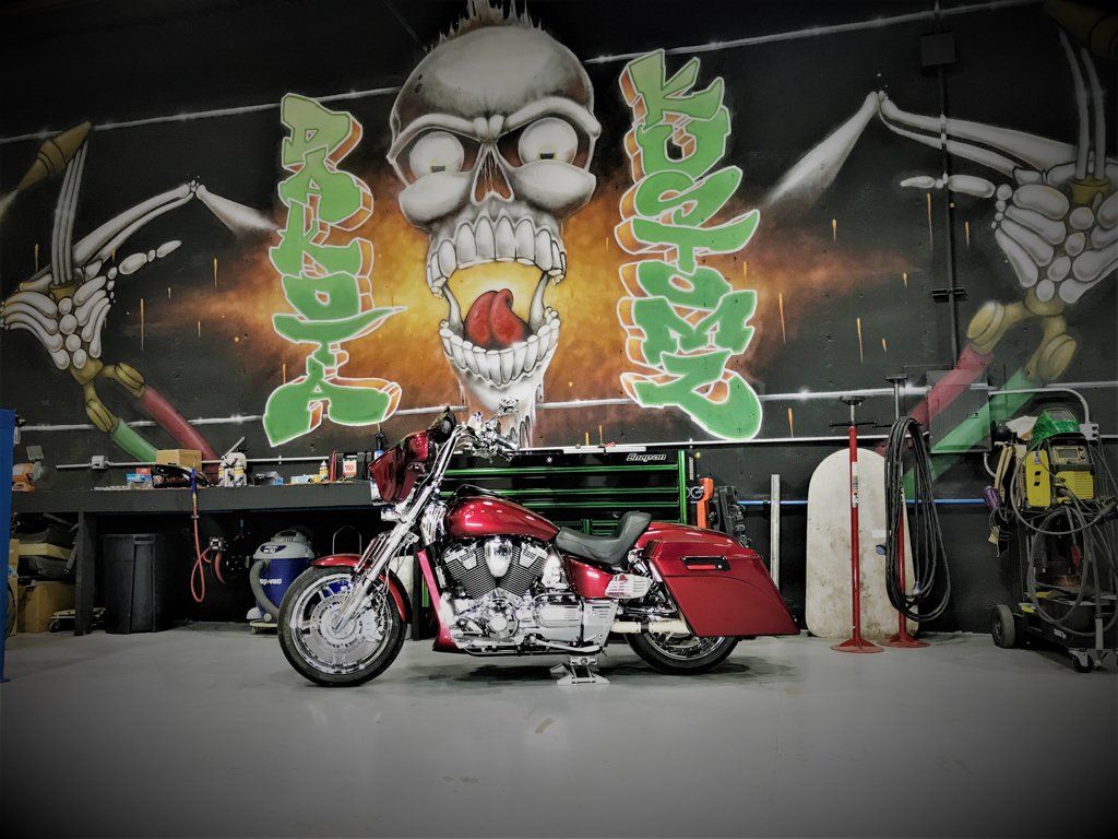 side view of rear view of customized red and chrome motorcycle in garage with dakota kustomz graffiti art in front of dakota kustomz graffiti art