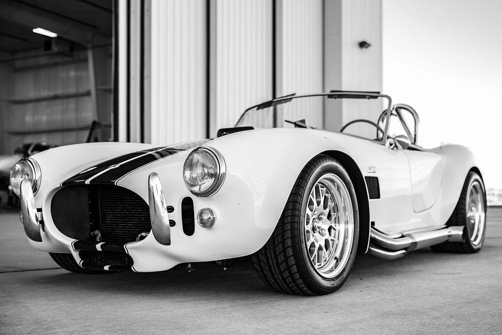 custom white 1965 shelby cobra hot rod in front of airplane hangar