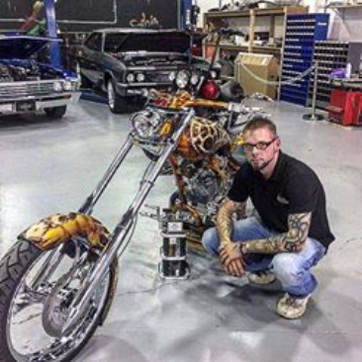 owner travis posing in front of custom yellow and orange custom motorcycle