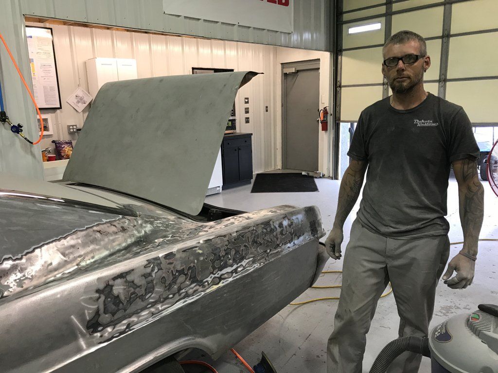 car rear with paint removed and mechanic in foreground