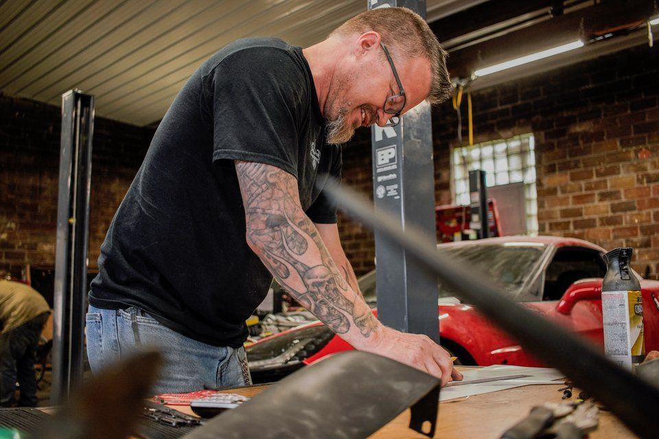 mechanic working on customization plans on workbench with red corvette in background