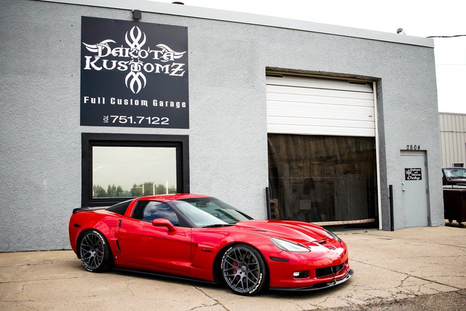 custom red 2006 corvette car in front of dakota kustomz store