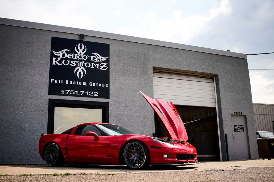 custom red 2006 corvette car with hood open in front of dakota kustomz store