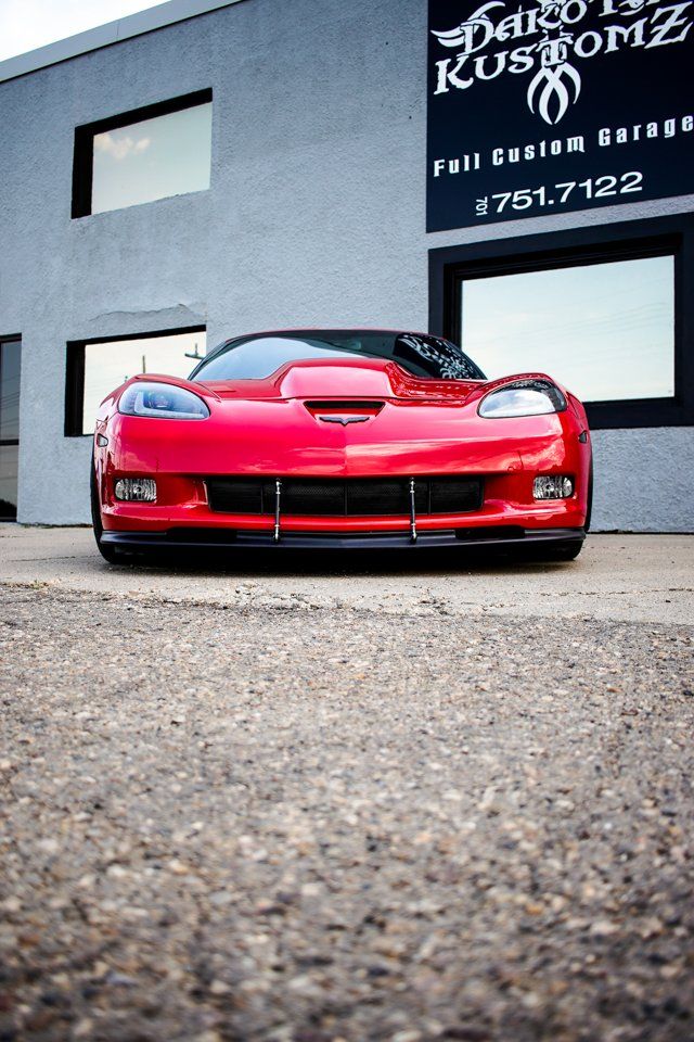 low front view of custom red 2006 corvette car in front of dakota kustomz store
