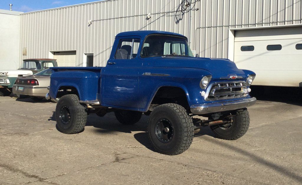 customized 1955 blue chevy pickup truck in front of dakota kustomz garage