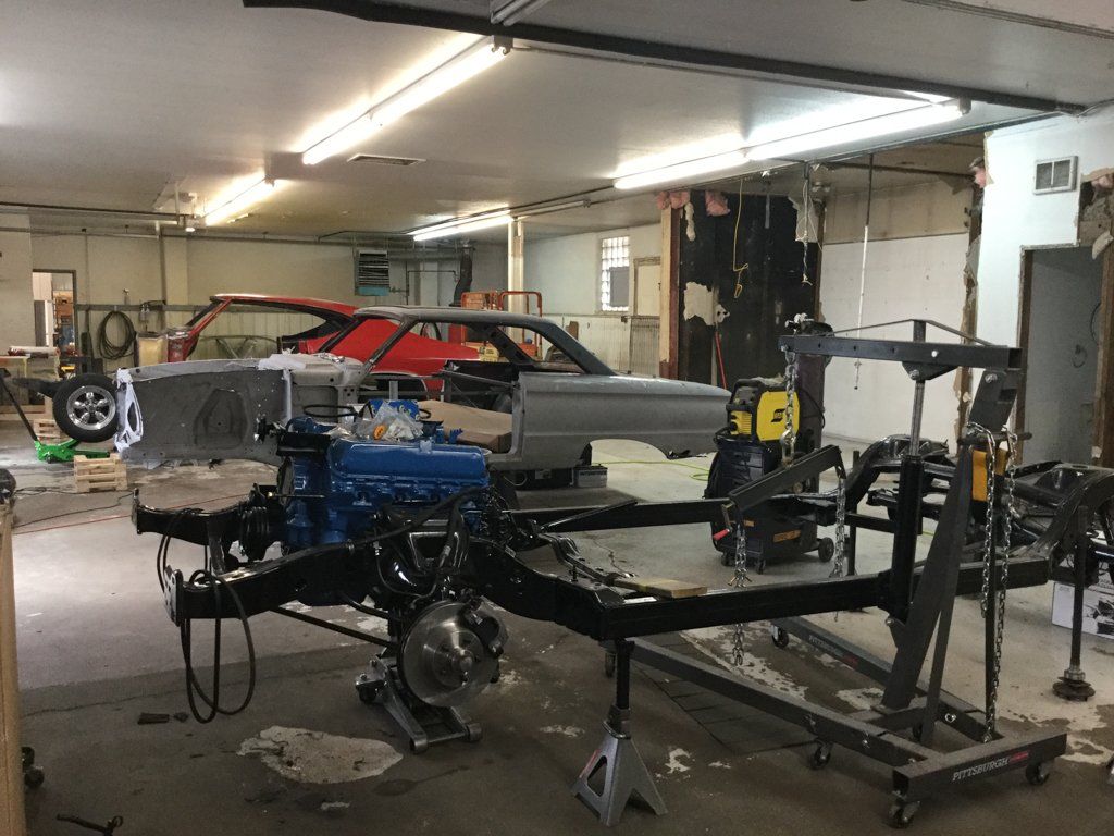 suspended engine next to chasis next to car body in garage