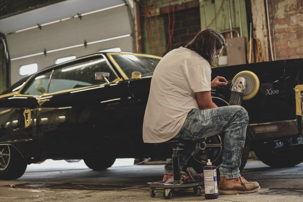 mechanic sitting on working stool detailing car