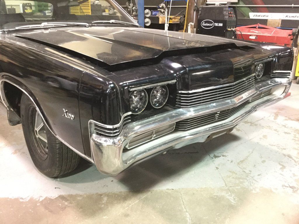 front closeup of black muscle car with hood slightly ajar in garage