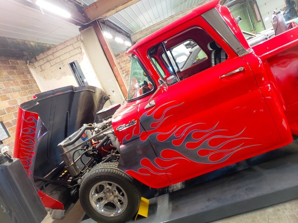 Side view of red customized 1962 truck with grey flames with lift kit on service bay