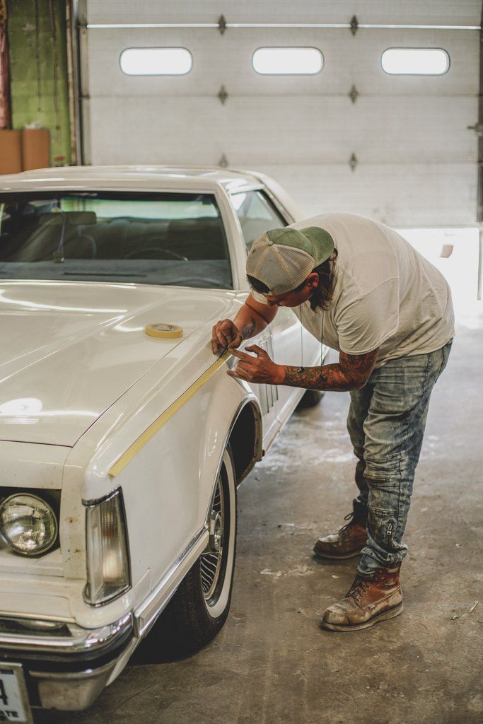 painter leaning over to hand paint pinstripe to white lincoln