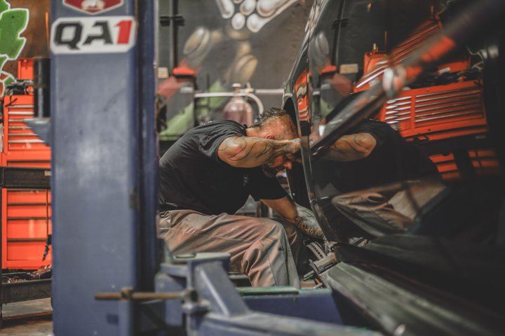 mechanic looking at wheels on black custom car in Dakota Kustomz shop