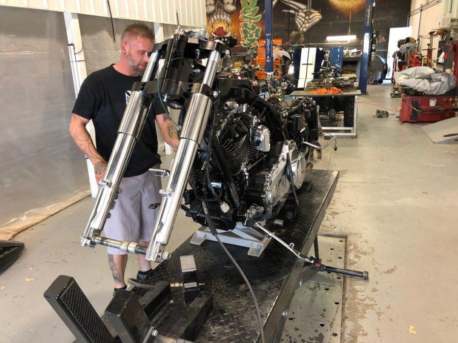 mechanic inspecting black custom chopper on service bay front wheel removed