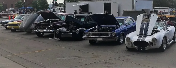outdoor line up of custom muscle cars and hot rods with hoods open