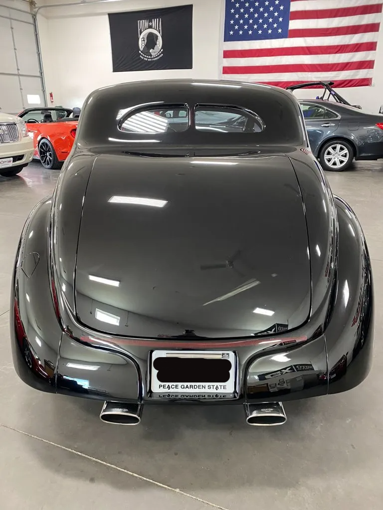 rear view of custom black 1937 ford tudor hot rod with american flag in background