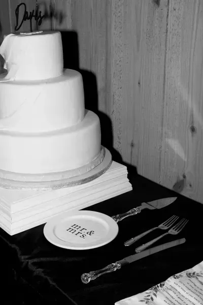 Three-tier white cake on a table with knife, forks, and a round plaque beside it