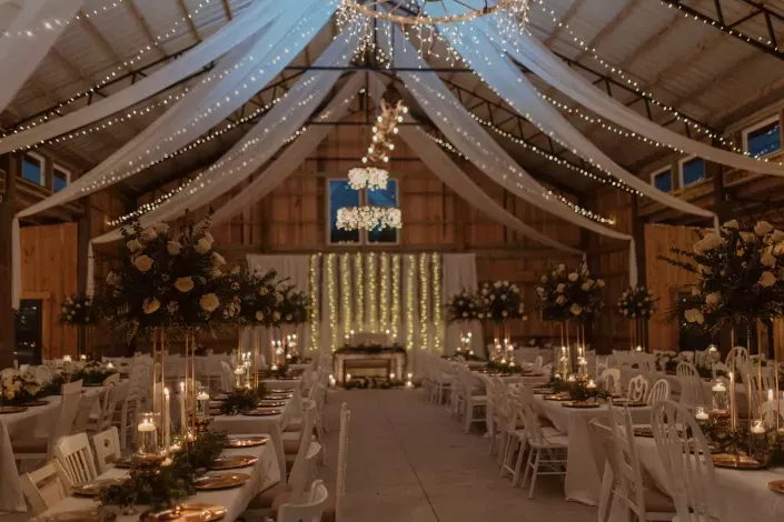 Decorated rustic wedding reception tent with draped lights, candles, and long banquet tables