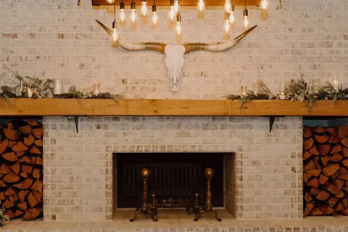 Stone fireplace with a wooden mantel, chandelier, and stacked firewood in a cozy living room