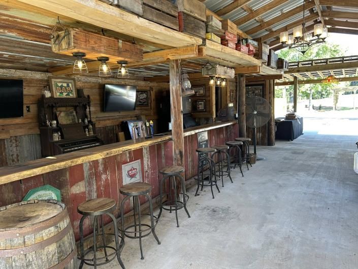 Rustic open-air bar with wooden stools, hanging lights, and a concrete floor under a timber roof
