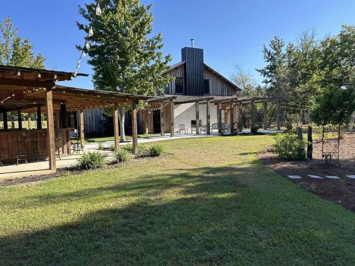 Courtyard with green lawn, wooden pergolas, and a rustic building under a clear blue sky