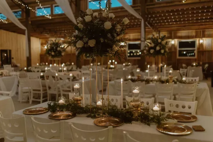 Elegant wedding reception hall with round tables, white chairs, candles, and tall floral centerpieces