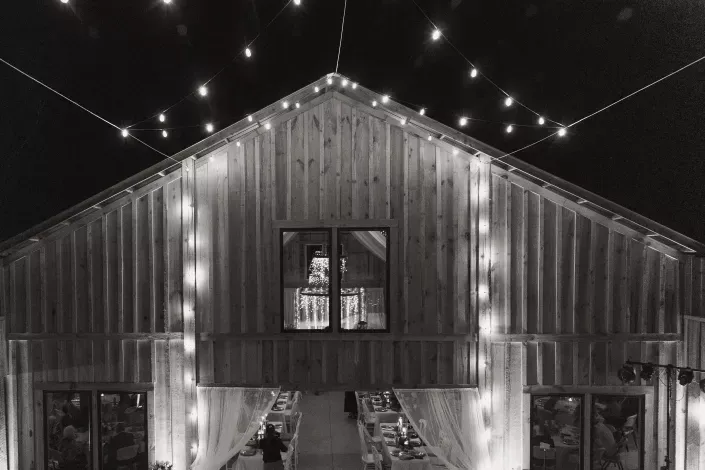 Black-and-white barn lit with string lights, with a person visible in the central upper window.
