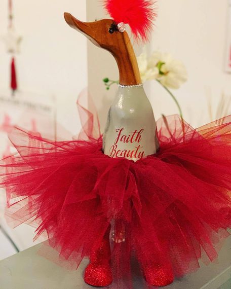 A wooden duck wearing a red tutu that says faith beauty