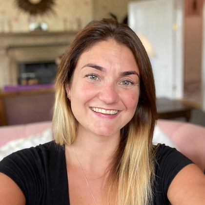 A woman in a black shirt is smiling for the camera while sitting on a pink couch.