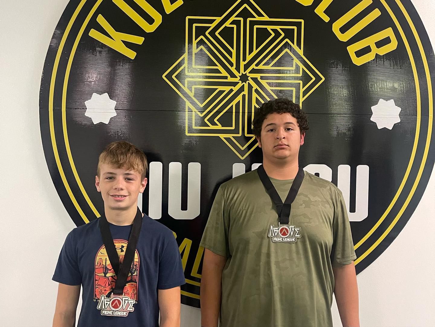 Two young men wearing medals are standing in front of a sign.