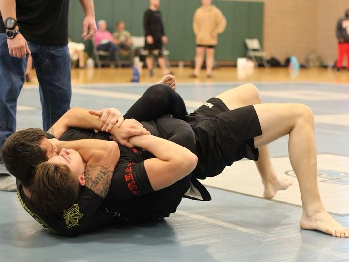 Two men are wrestling on a mat and one has a tattoo on his arm