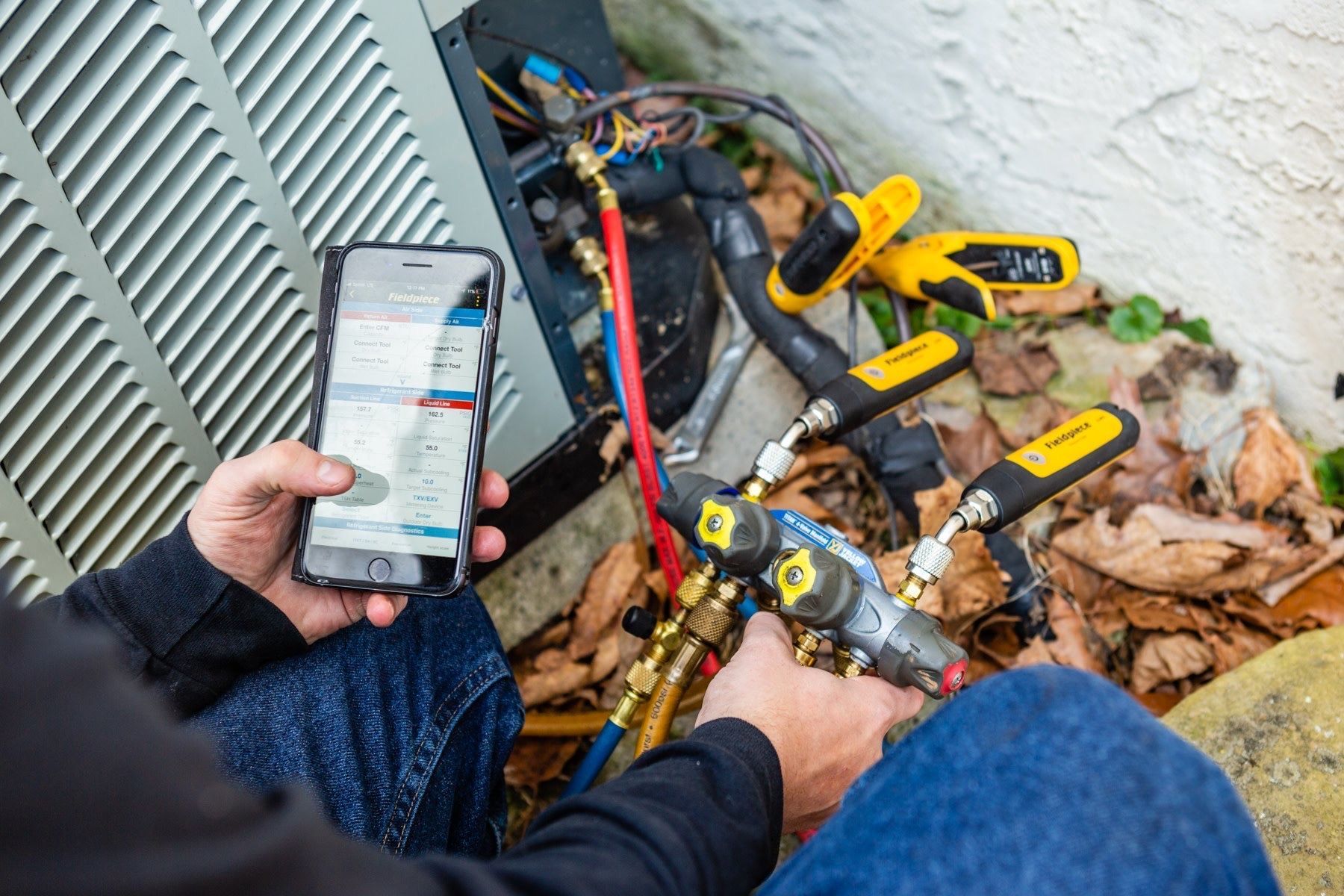 A man is using a cell phone while working on an air conditioner.