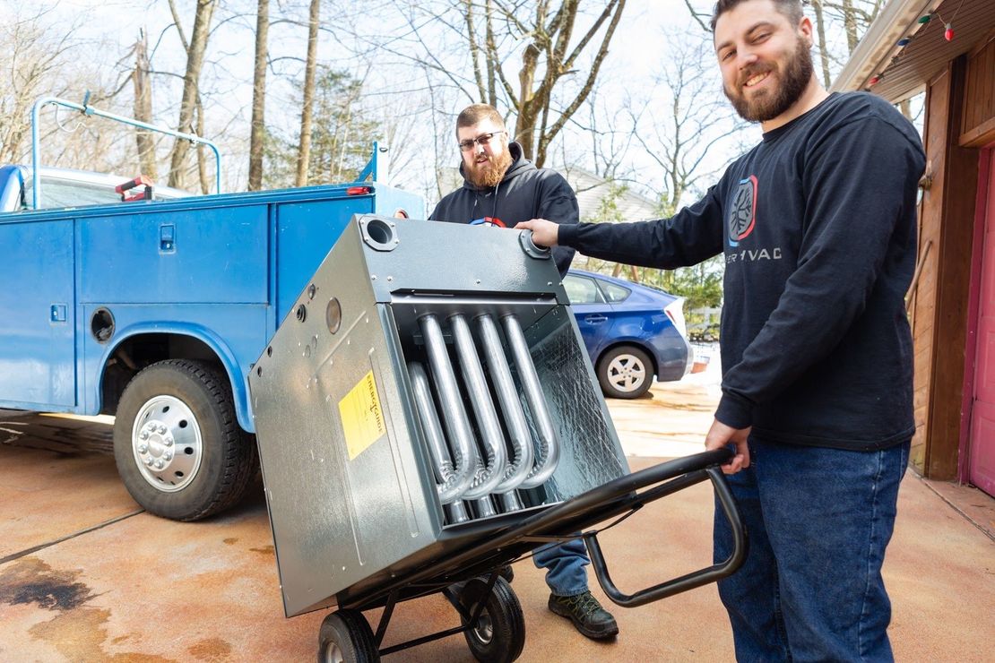 Two men are carrying a large piece of metal on a hand truck.