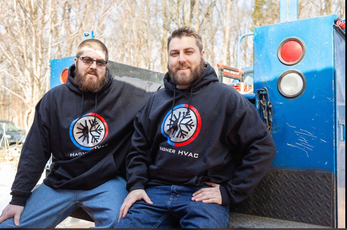 Two men are sitting on the back of a truck wearing hoodies that say hvac