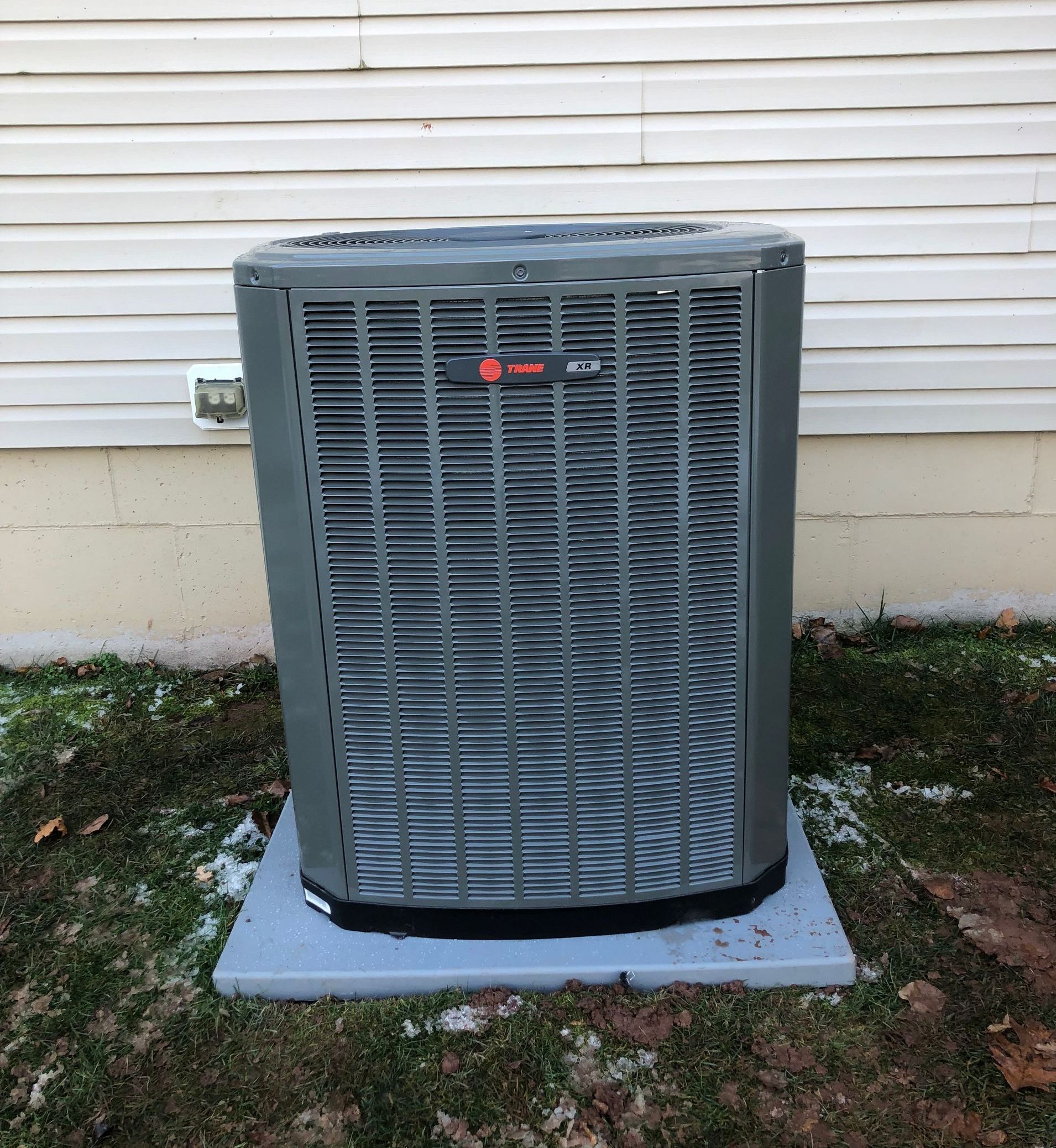 A large air conditioner is sitting on top of a concrete platform in front of a house.