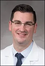 A smiling doctor in a lab coat with a stethoscope around his neck.