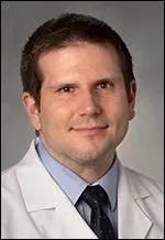 A smiling doctor in a lab coat with a stethoscope around his neck.