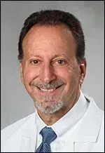 A smiling doctor in a lab coat with a stethoscope around his neck.