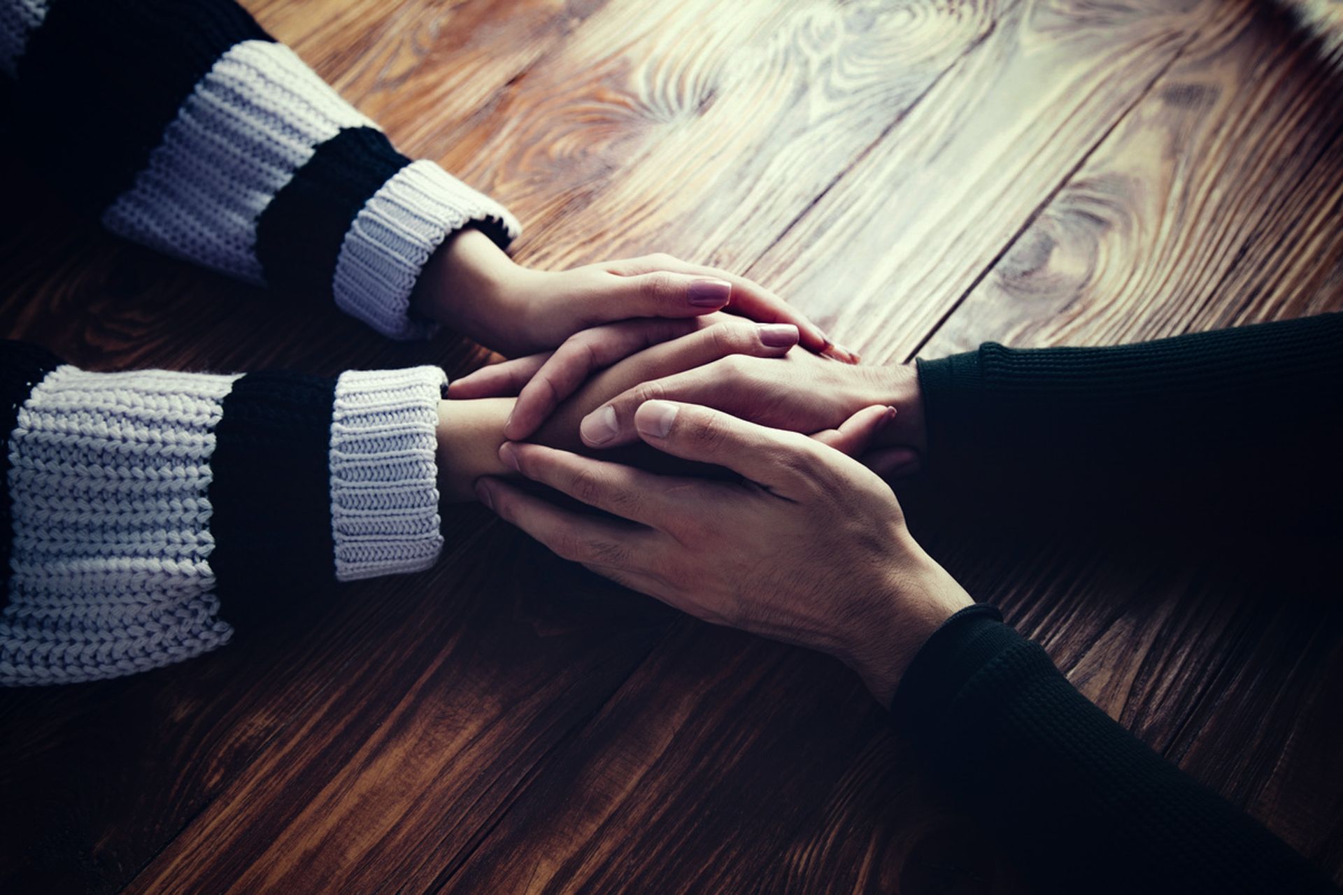 Three hands gently stacked together on a wooden table, wearing dark and striped sweaters
