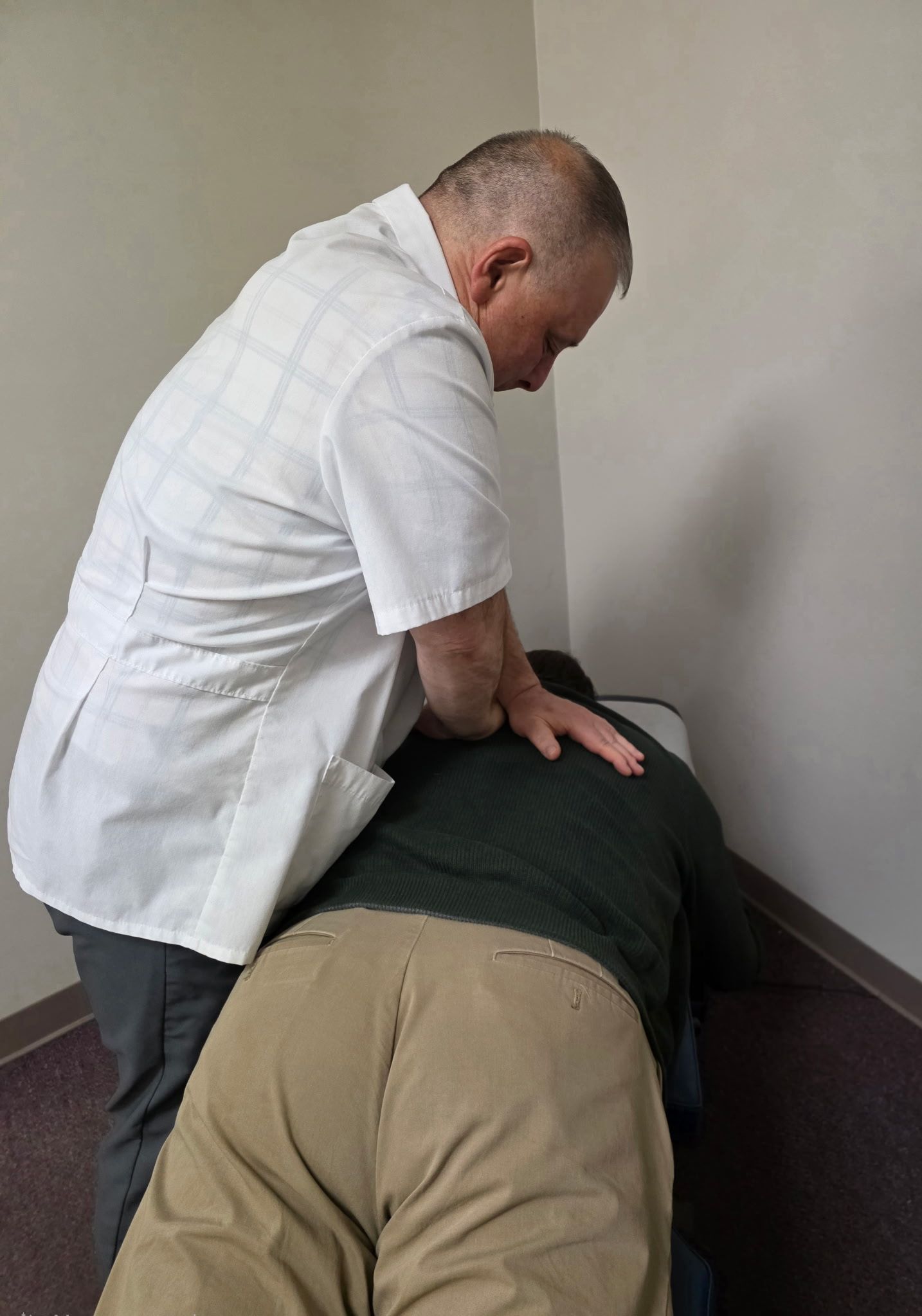 Chiropractor adjusting a patient's back on a table. The doctor wears a white coat and the patient is face down.