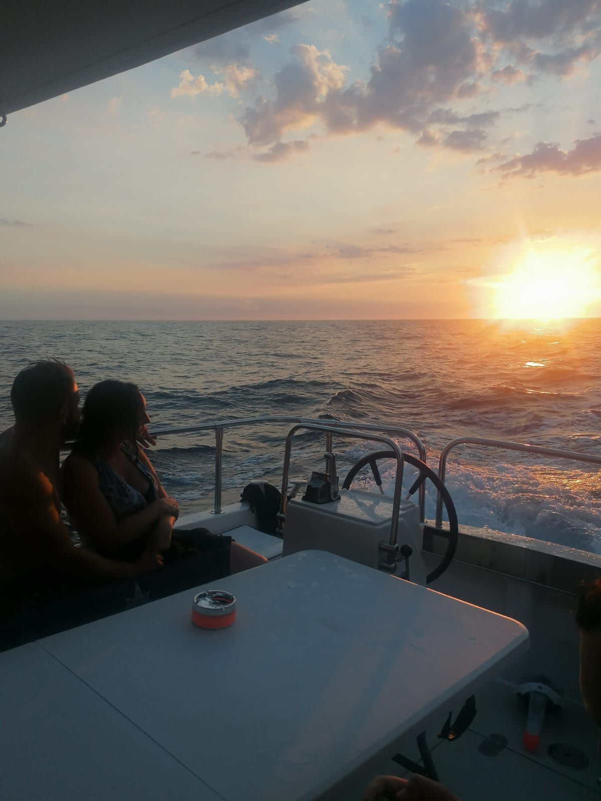 Un uomo e una donna sono seduti su una barca e guardano il tramonto sull'oceano.