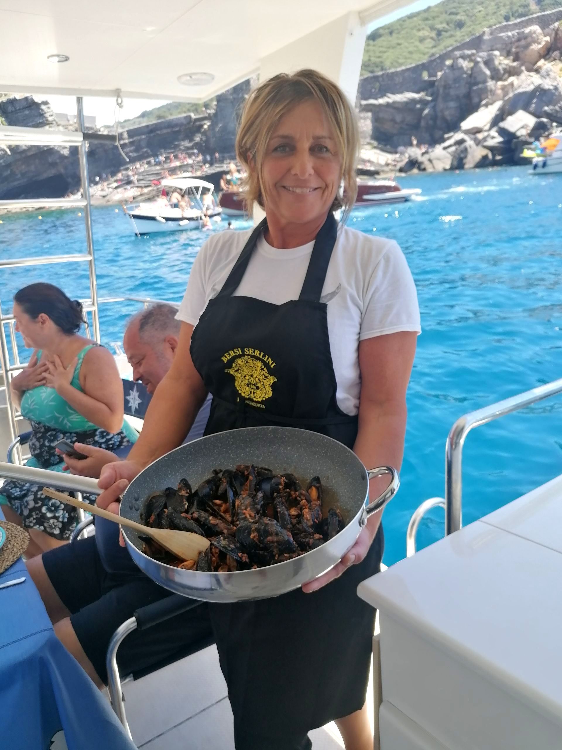 Una donna con un grembiule tiene in mano una pentola di cibo su una barca