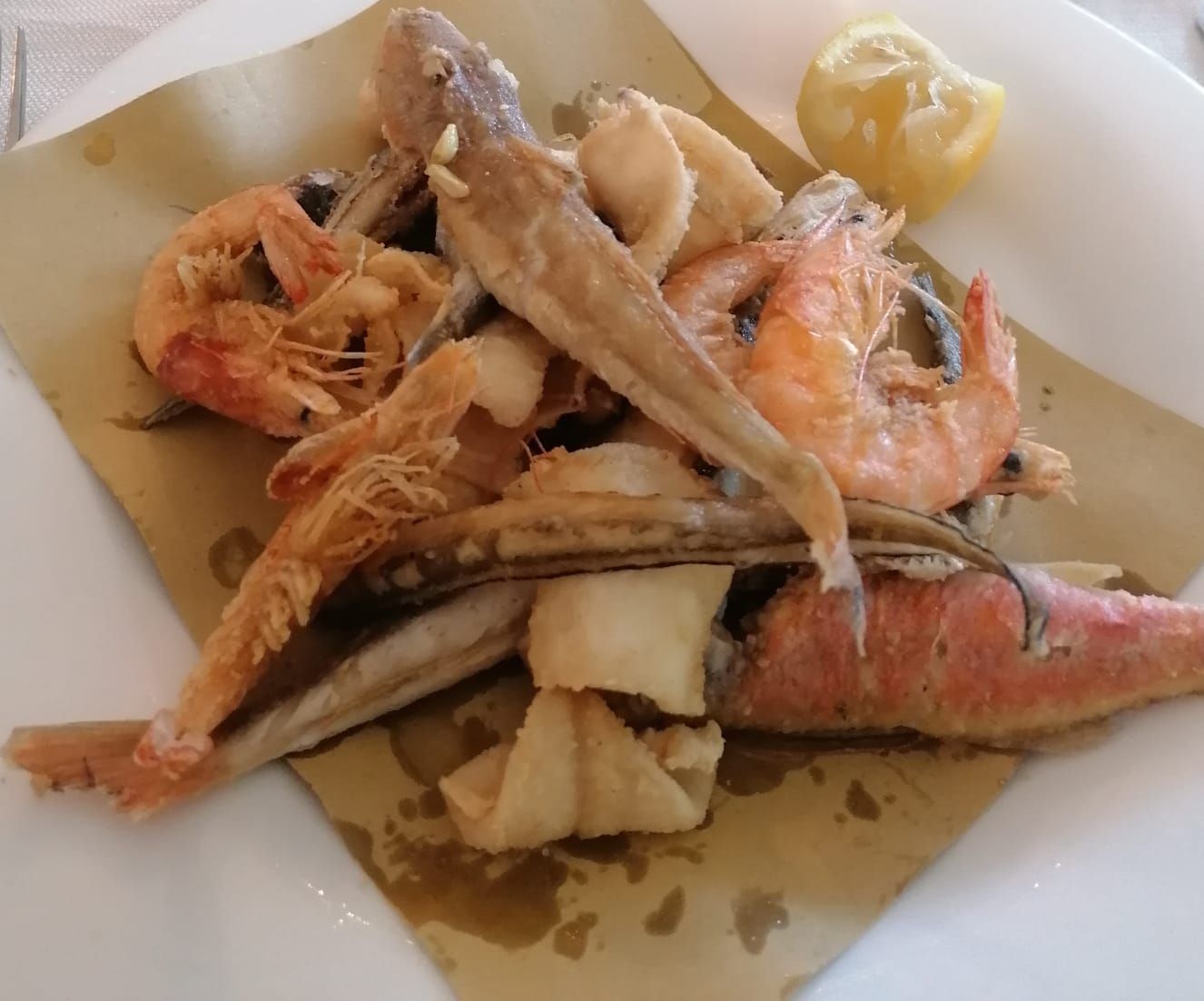 Un piatto bianco condito con frutti di mare fritti e uno spicchio di limone