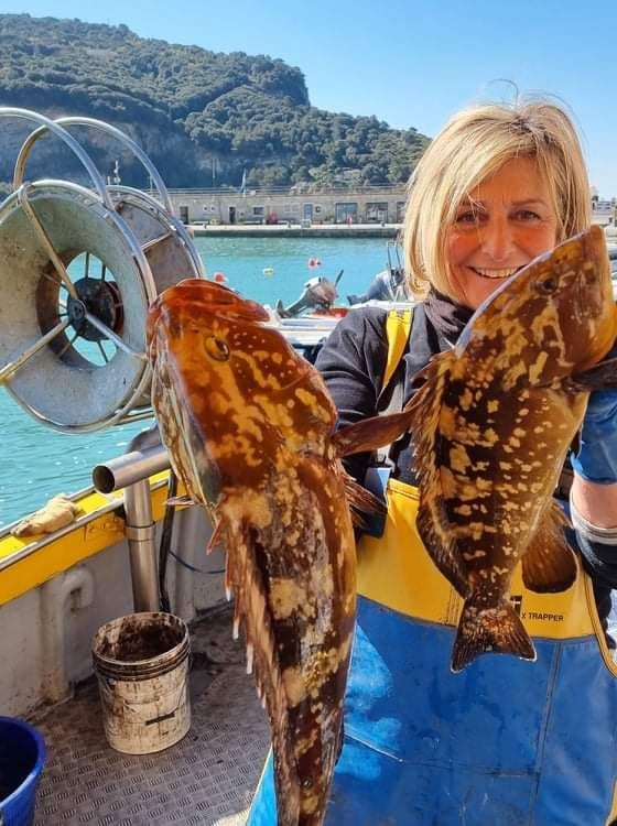 Una donna tiene in mano due grossi pesci su una barca.