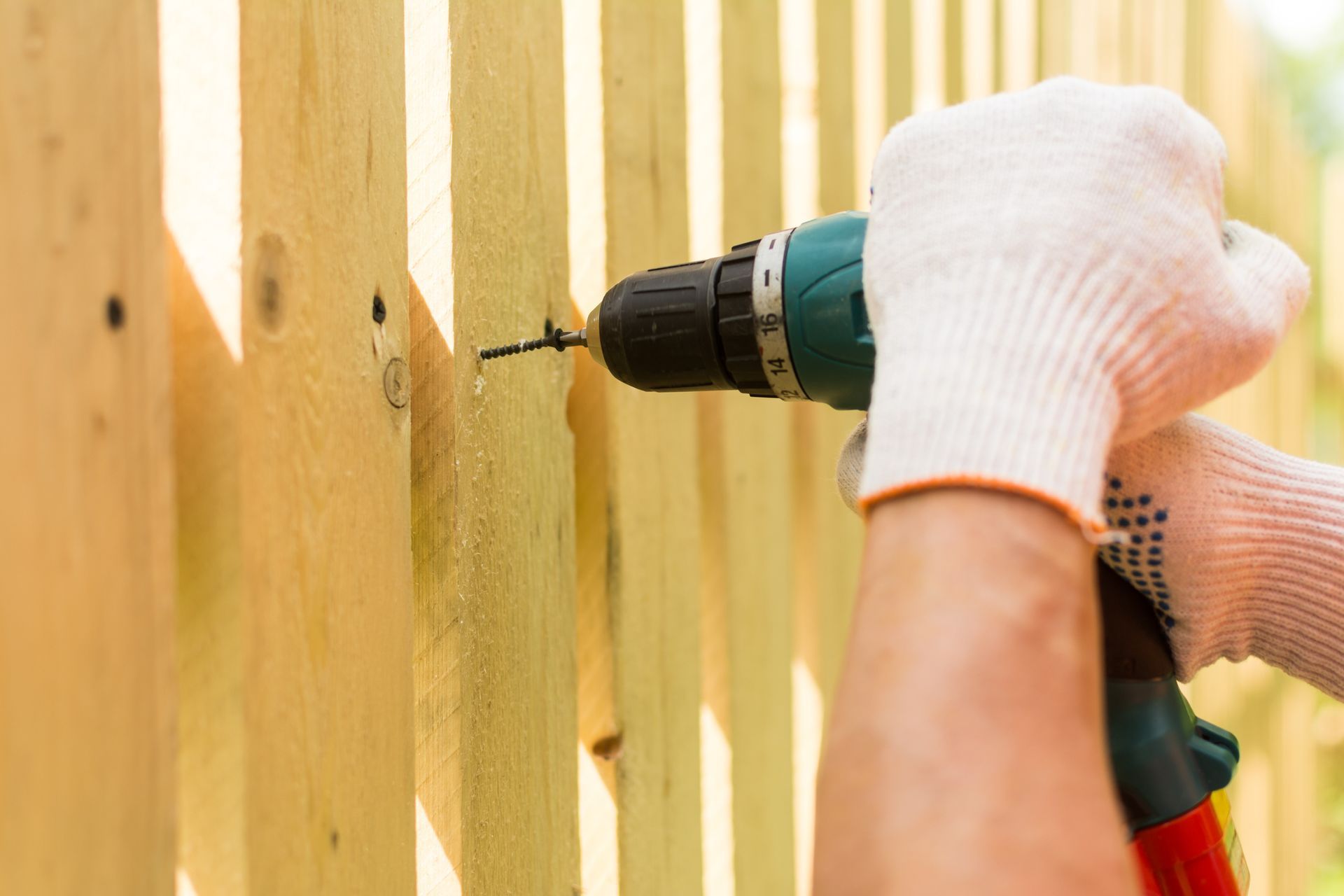 Close-up of a contractor's hands in white gloves, holding a screwdriver for fence installation.