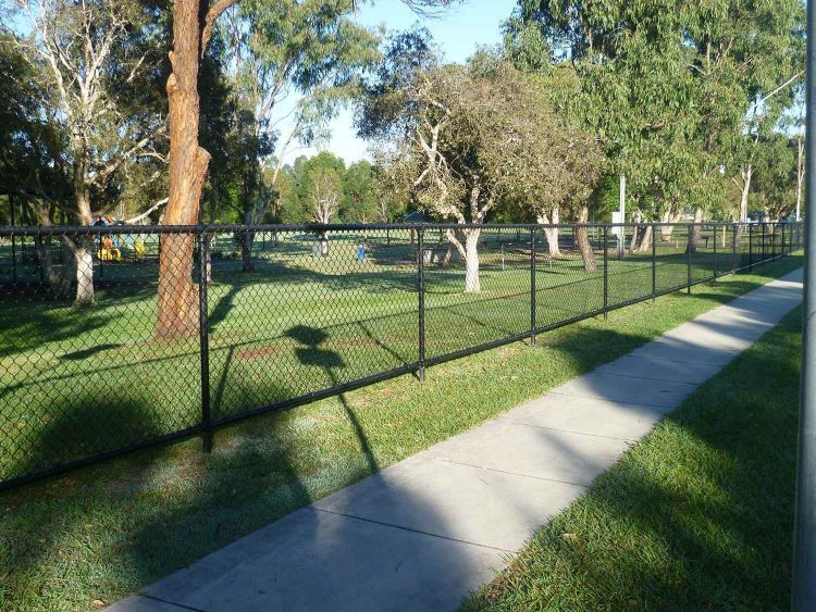 A chain link mesh fence along a sidewalk in a park