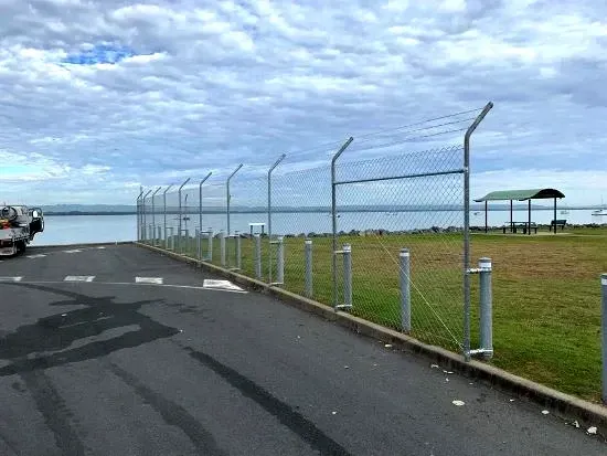 A mesh fence surrounds a grassy field next to a body of water.
