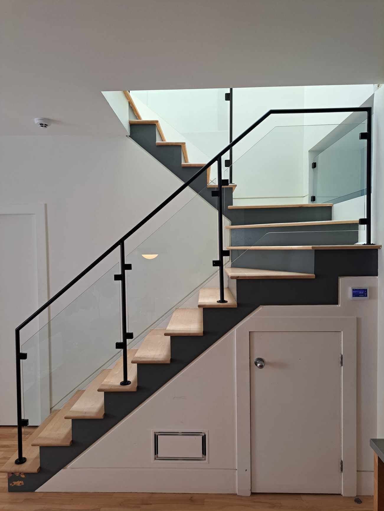 A staircase with a glass railing and a door underneath it.