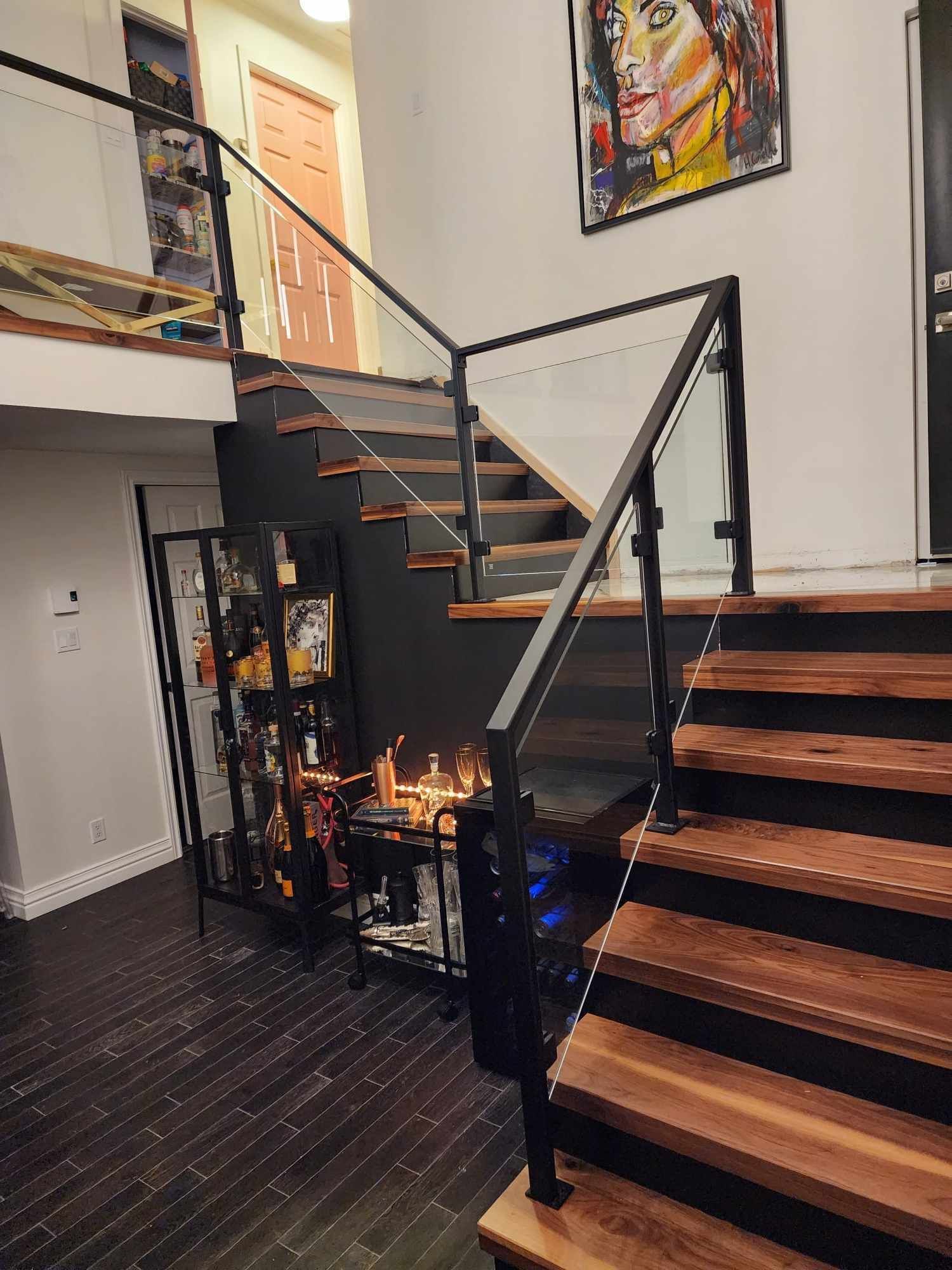A wooden staircase with a glass railing and a painting on the wall.