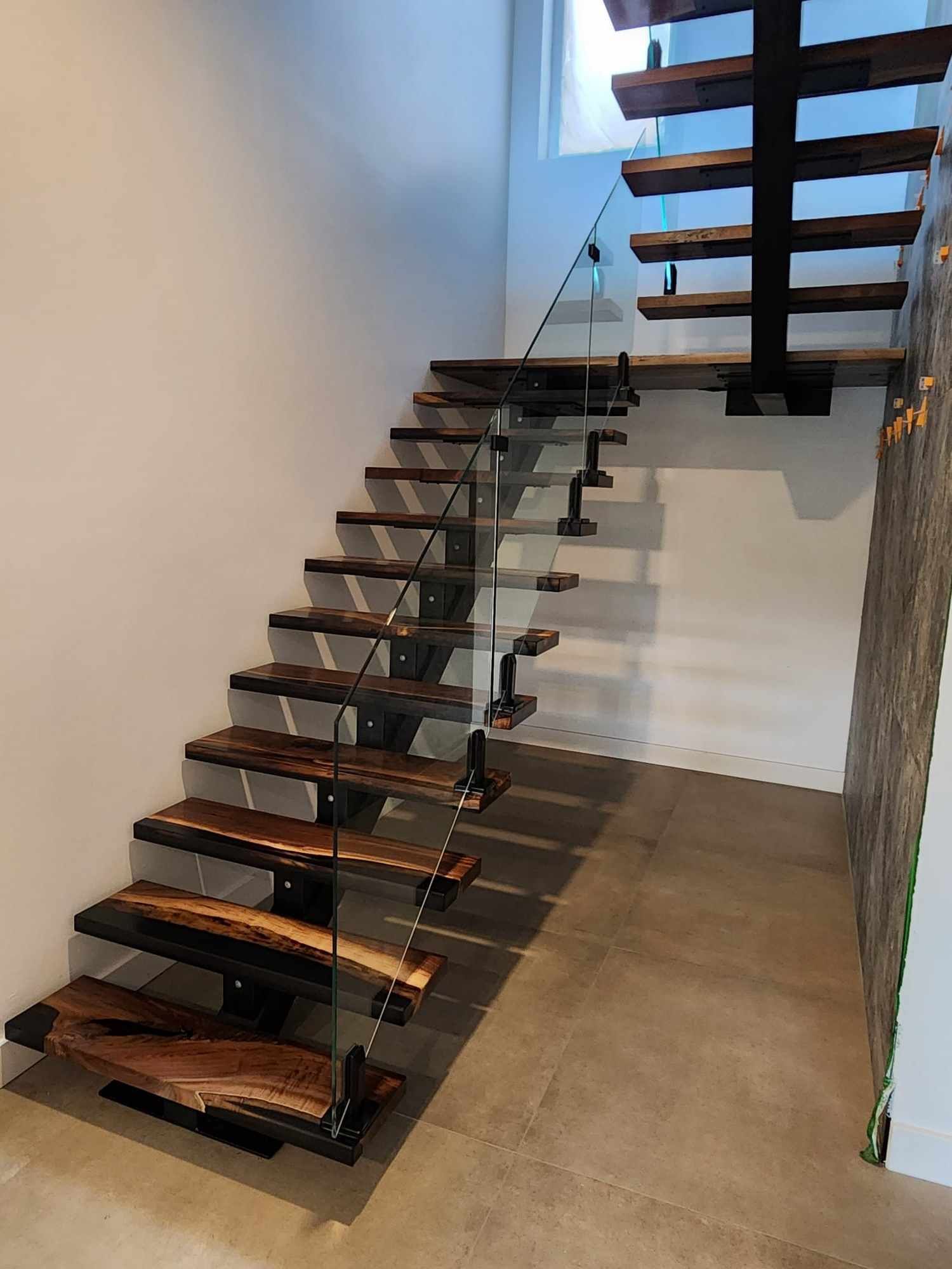 A wooden staircase with a glass railing in a hallway.